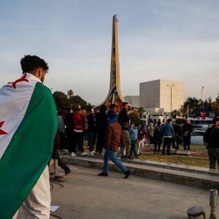 Ein Mann mit Revolutionsflagge auf dem Rücken geht über einen Platz in Damaskus.