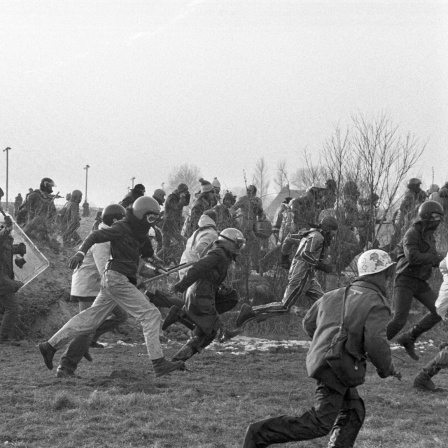 Polizisten mit Schutzschilden und Schlagstöcken rennen 1981 flüchtenden Atomkraftgegnern mit Schutzhelmen hinterher. (Archivbild)