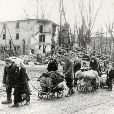 Flucht aus den deutschen Ostgebieten vor den vorrückenden Truppen der Roten Armee im Frühjahr 1945: eine Gruppe von Flüchtlingen mit Handwagen in einer zerstörten Ortschaft in Ostpreußen
