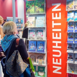 Die ersten Besucher schauen auf die Neuerscheinungen auf der Buchmesse. Sie stehen in einem großen Regal.