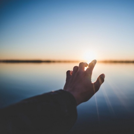 Eine Hand streckt sich in Richtung Horizont und Sonnenlicht.
