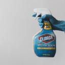 Eine Hand in Putzhandschuh hält eine Chlorbleiche zum sprühen.