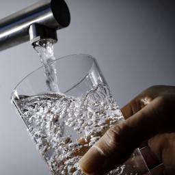 Wasser fließt aus einem Wasserhahn in ein Glas
