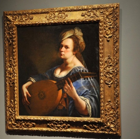  Artemisia Gentileschis Gemälde "Selbstporträt als Lautenspielerin". Eine Frau des Barock spielt eine Laute und schaut in Richtung des Betrachters.