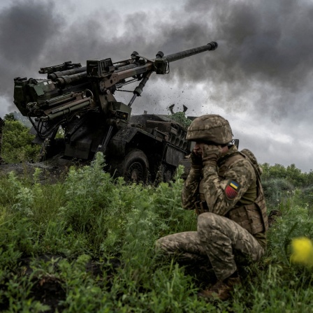 Zwei ukrainische Soldaten feuern auf einem grünen Hügel eine Haubitze ab