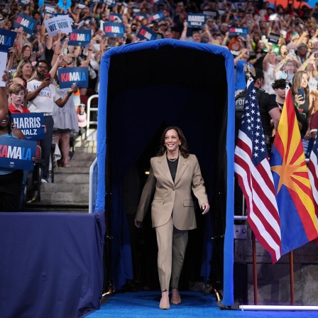 Die demokratische Präsidentschaftskandidatin und US-Vizepräsidentin Kamala Harris geht durch ein blaues Tor bei einer Wahlkampfveranstaltung in Glendale, Arizona. Um sie herum Fahnen und Fans, 9. August 2024.