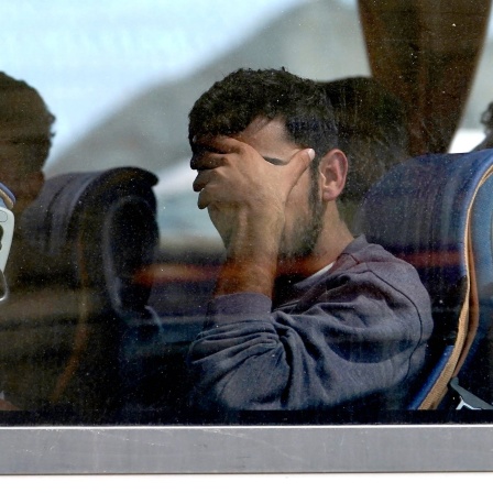 Ein junger Mann sitzt in einem Bus und verbirgt sein Gesicht hinter seiner linken Hand, nachdem Grenzbeamte ihn und andere mutmaßliche Migranten an der französisch-britischen Grenze festgesetzt hatten.