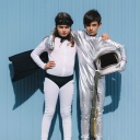 Zwei Kinder in Superhelden-Kostümen stehen vor einer blauen Hauswand