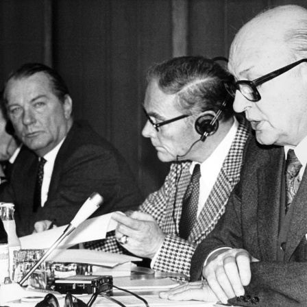 Wehrkundetagung in München 1978: Ein Mann im Vordergrund spricht in ein Mikrofon, mehrere Tischnachbarn hören ihm zu.