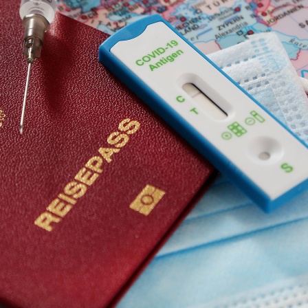 Reisepass, Schutzmaske, Schnelltest und Spritze auf einer Landkarte