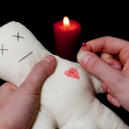 ILLUSTRATION: Eine Frau steckt steckt eine Nadel ins Herz einer Voodoo-Puppe.