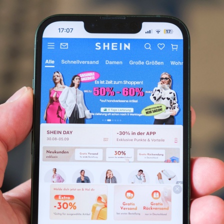 Hand hält Mobiltelefon auf der die Website des chinesischen Unternehmens Shein zu sehen ist.