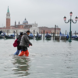 Mehrere Personen waten durch Wasser auf der überfluteten Piazza San Marco in Venedig.