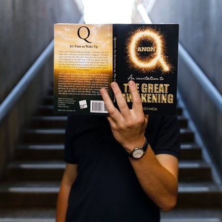 Ein Mann hält sich das Buch QAnon- The great Awakening vor das Gesicht 5.7.2020