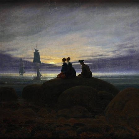 Digitale Reproduktion des Gemäldes Mondaufgang am Meer" (1822) von Caspar David Friedrich (1774 -1840). Zu sehen sind zwei Frauen und ein Mann, die auf einem Felsen im Mondschein sitzend auf in der Ostsee ankernde Segelschiffe schauen. 