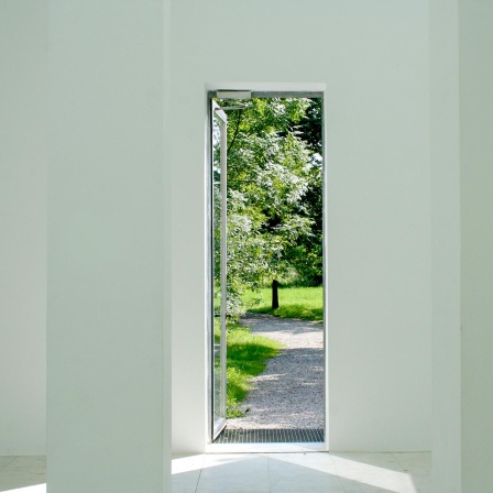 Blick aus einem Gebäude durch eine Türe in einen Garten bei sommerlichem guten Wetter