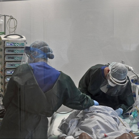 Zwei Krankenhausmitarbeitende stehen an einem Intensivbett und kümmern sich um einen Patienten.