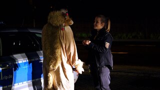 Junge Polizeibeamtin spricht mit einer verkleideten Person