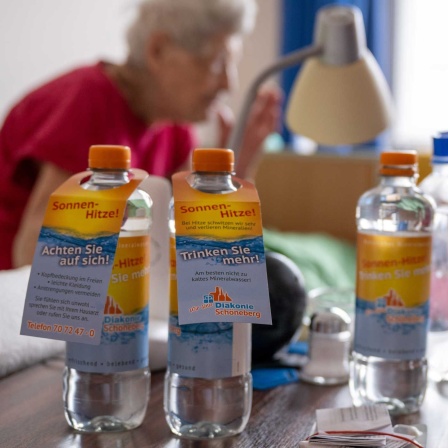 Wasserflaschen mit der Aufschrift "Sonnenhitze! Achten Sie auf sich! Trinken Sie mehr!" auf einem Tisch einer pflegebedürftigen Seniorin (Bild: picture alliance/dpa/Monika Skolimowska)