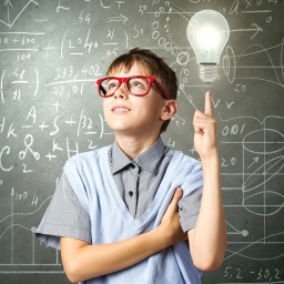 Junge mit Brille steht symbolisch vor einer Tafel mit mathematischen Formeln, Glühbirne