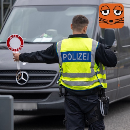 Ein Polizist hält eine Polizeikelle vor einen Lieferwagen. Auf der Polizeikelle steht: Halt, Polizei.