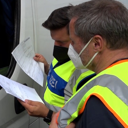 Zwei Polizisten kontrollieren die Dokumente eines Fahrers bei seiner Einreise nach Deutschland.