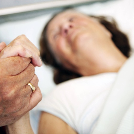 Hand einer alten Frau im Krankenbett wird gehalten