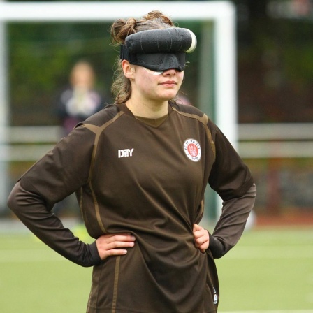 Blindenfußballerin Thoya Küster während eines Spiels für den FC St. Pauli mit Sichtschutz vor den Augen. Ihre Hände hat sie in die Hüften gestemmt.