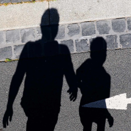 Der Schatten von einem Mann und einem Kind sind auf einer Straße mit einem Pfeil zu sehen.