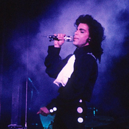 Prince singt auf der Bühne in purpurem Licht.