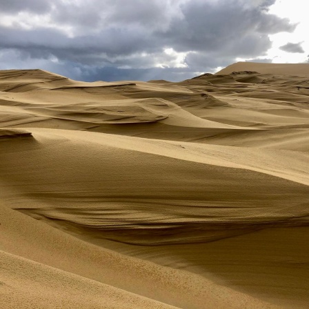 Europas höchste Düne, die Dune du Pilat. Ein großer Sandberg vor einem wolkenschweren Himmel.