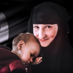 Leonora trägt ein Kopftuch und hält ein Kind auf dem Arm. Im Hintergrund eine Flagge mit arabischen Schriftzeichen.