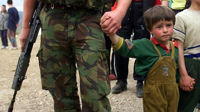 Ein NATO-Soldat hält die Hand eines kosovarischen Jungen.