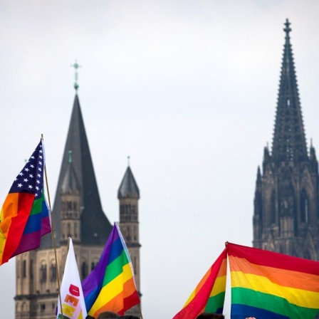 Regenbogen Fahnen im Vordergrund. Dahnter ist verschwommen der Kölner Dom zu sehen.