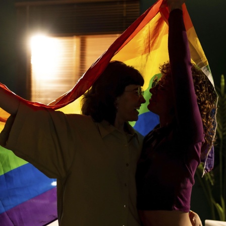 Silhouette eines romantischen Paares, das gemeinsam eine Regenbogenflagge hält.