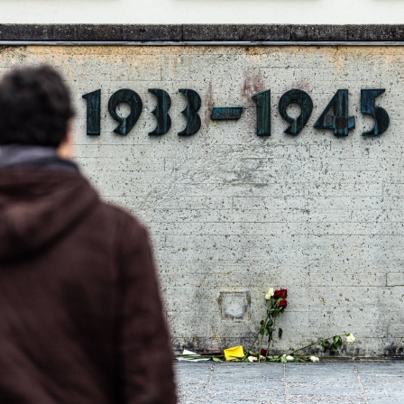 Rosen liegen am Boden vor einer Mauer des KZ Dachau auf der die Jahreszahlen "1933 - 1945" angebracht sind