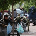 Zwischen lokalen Polizeikräften sind KFOR Soldaten in Tarnuniformen zu sehen, die Natodraht ausrollen.