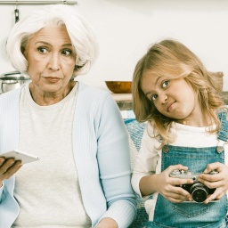 Eine Oma und ihre Enkelin sitzen auf einem Sofa und rätseln.
