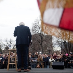 Rückansicht von Bernie Sanders, der während einer Ansprache vor Publikum an einem Pult steht.