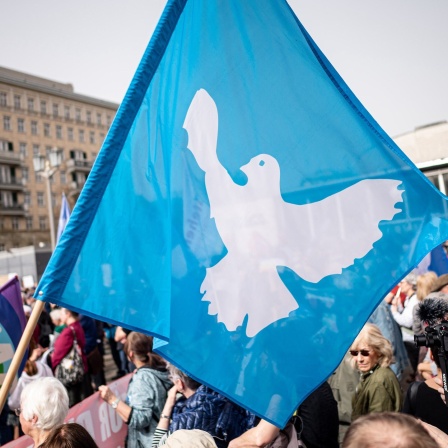 Demonstranten halten Fahne mit Friedenstaube hoch