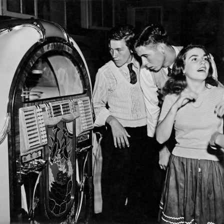 Schwarz-weiß Bild aus den 1950er-Jahren. Junge Menschen stehen vor einer Jukebox.