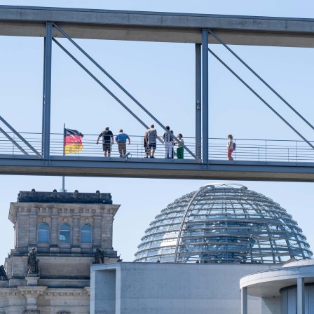 Menschen stehen auf dem Marie-Elisabeth-Lüders-Steg im Berliner Regierungsviertel und blicken auf das Reichstagsgebäude.