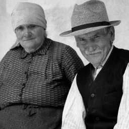 Altes Ehepaar sitzt auf einer Bank und schaut in die Kamera.