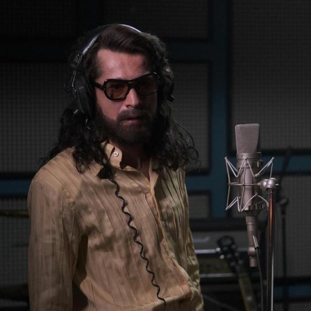 Im Still aus "Cem Karaca" steht der Protagonist mit langen Haaren und in einem seidenen Hemd in einem Aufnahmestudio neben dem Mikrofon.