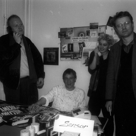 Frieder Butzmann steht mit zwei Männern und einer Frau um einen Tisch.