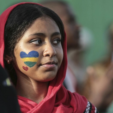 Aufnahme einer Frau mit einem geschminkten Herz auf der Wange in den Farben der alten sudanesischen Flagge.