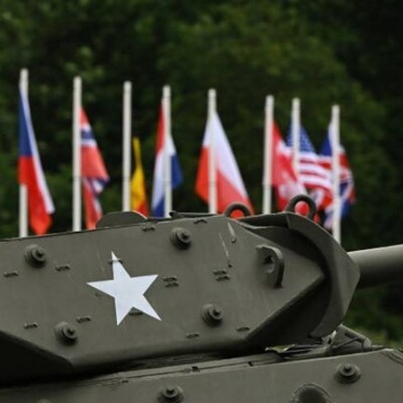 Hinter einem Panzer mit weißem Stern stehen aufgereiht die Flaggen aller westlichen Alliierten Länder, die bei der Landung in der französischen Normandie teilgenommen haben