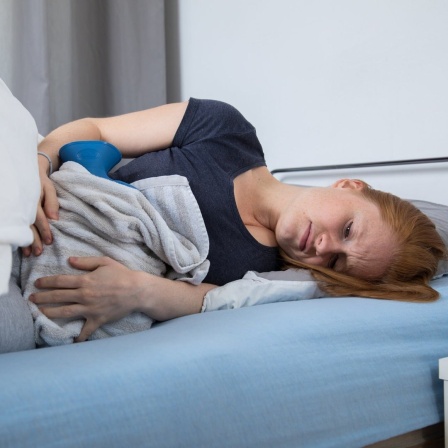 Eine junge Frau liegt in einem Bett und leidet unter Bauchschmerzen.