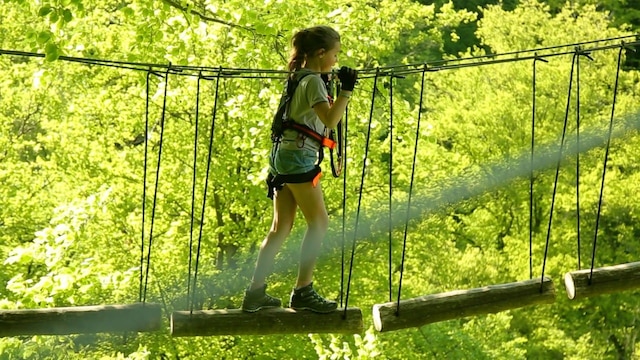 Ein Kind geht über eine Brücke in einem Kletterwald
