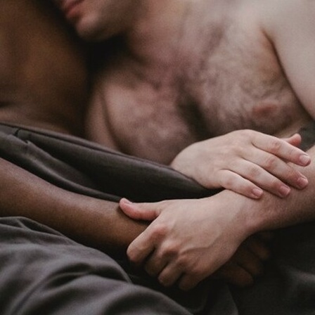 Zwei unbekleidete Männer halten sich im Arm im Bett